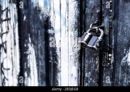 Old black metal padlock on a black and white wooden door Stock Photo