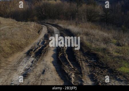 Bad muddy countriside road in spring. Closeup of the dirty country road after the snow melts or rain. Muddy path with tire tracks among the hills Stock Photo