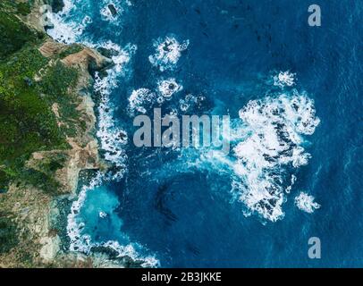 Aerial View of Waves Breaking on Rock. Light and dark blue water foaming whilst waves break to the shore. Deep Sea. Stock Photo
