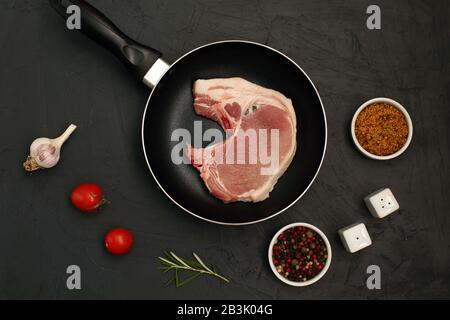 Raw pork loin chops in rustic skillet on black background Stock Photo