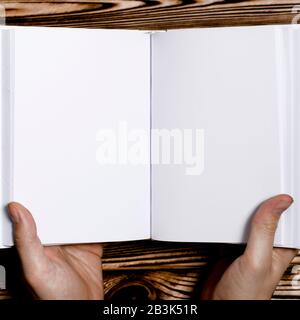 Men's hands holding open book with blank cover on light background. Mockup of open blank square book Stock Photo