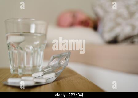 Sick man lying in bed with pills and glass of water on foreground Stock Photo