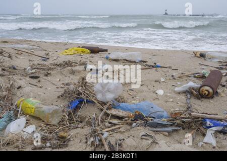 Spilled garbage on the beach of the big city. Empty used dirty plastic bottles, bags and other rubbish on the seashore. Stock Photo