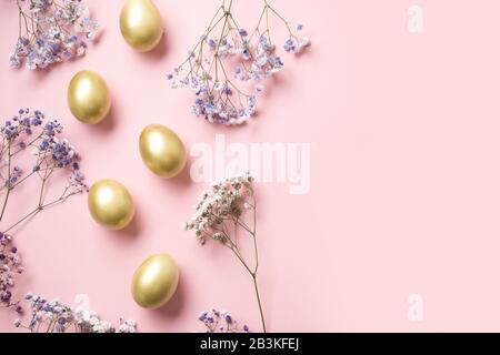 Easter frame of golden eggs flowers and gypsophila on pastel pink. Top view. Happy Easter holiday. Greeting card with copy space. Stock Photo
