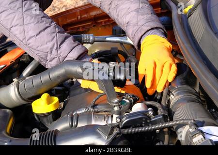 Automobile maintenance concept. Hands of driver in orange rubber gloves checks car, open hood. Cars and transportation, close up. Stock Photo