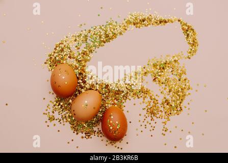 Easter holiday brown eggs in a large pile of shiny gold stars on a delicate pink background. Easter layout in art Deco style Stock Photo