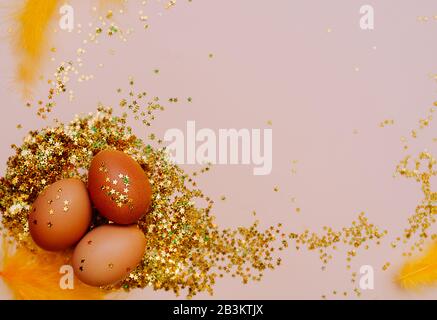 Easter holiday brown egg in a large pile of shiny gold stars on a delicate pink background. Happy Easter minimalism mockup, flat lay Stock Photo