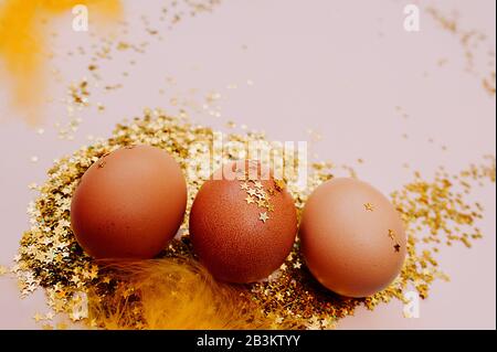 Easter holiday brown egg in a large pile of shiny gold stars on a delicate pink background. Happy Easter minimalism mockup, flat lay Stock Photo