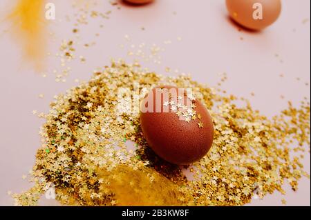 Easter holiday brown egg in a large pile of shiny gold stars on a delicate pink background. Happy Easter minimalism mockup, flat lay Stock Photo