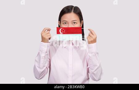 Asian woman wearing hygienic face mask painting Singapore flag to protect from the Coronavirus 2019 (COVID-19) infection outbreak situation, the virus Stock Photo