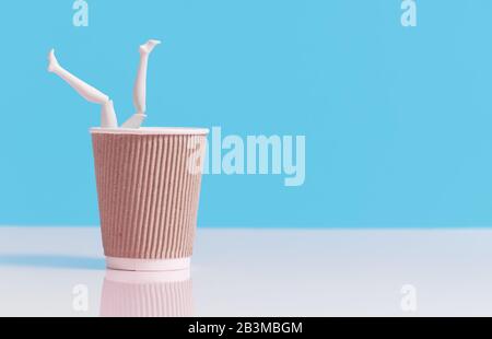 Time to drink some coffee. Female legs peek out from a coffee paper craft cup on a light blue background. Nearby is a pink alarm clock. Stock Photo