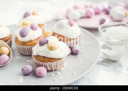 Glazed Easter cupcakes decorated with mini chocolate eggs candy on white marble background. Happy Easter Holidays. Stock Photo