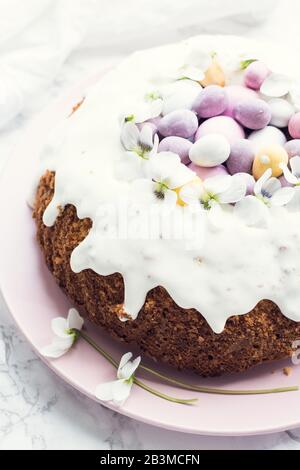 Glazed easter cake decorated with flowers and mini chocolate eggs candy on white marble background. Happy Easter Holidays. Stock Photo