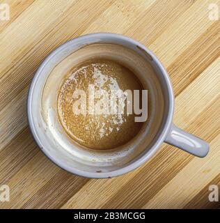 This scene features a coffee cup freshly drunken with a bit of sugar left on the bottom, the empty cup sits on a wooden chop board. Stock Photo
