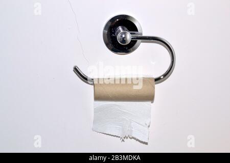The last sheet of toilet roll on an almost empty toilet paper roll holder on a toilet or restroom wall Stock Photo