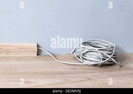 Internet web cable RJ 45 in the baseboard along the gray wall in the room. Stock Photo