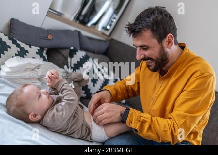 Father and baby.Young dad is changing baby diaper.Happiness and harmony in family life.Family, love,happiness and people concept. Stock Photo