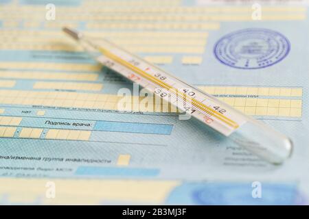 The thermometer is on the sick list- a document about temporary disability. Inscription in Russian signature of the doctor. Healthcare in Russia Stock Photo