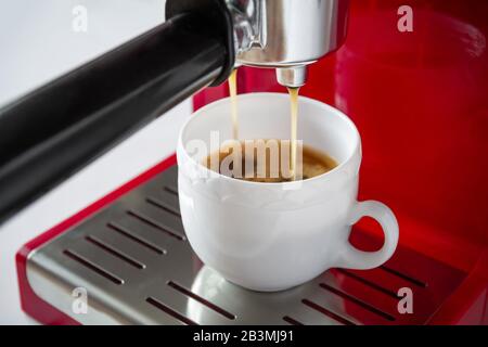 Espresso coffee pouring from machine at home into white cup. Closeup, selective focus Stock Photo