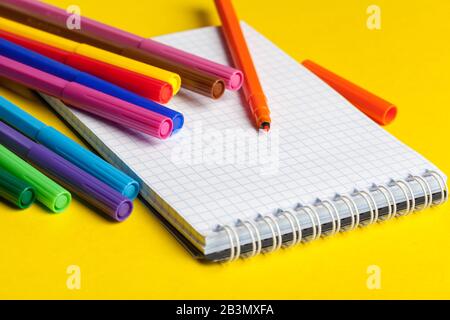 Felt-tip pens and blank notepad on bright yellow background Stock Photo
