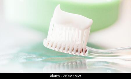 Plastic toothbrush with white toothpaste on a glass table and green soap background Stock Photo