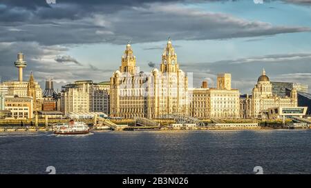 Liverpool waterfront with Mersey Ferry Royal Iris crossing to Pier head and Liver buildings and the iconic 3 Graces buildings. England UK Stock Photo