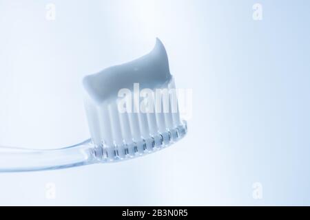 Transparent plastic toothbrush with white toothpaste on a light blue background. Stock Photo