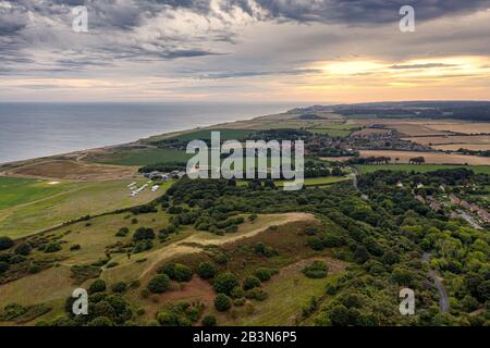 Aerial view of Muckleburgh Hill and Weybourne in Norfolk, the sun rising above Sheringham in the distance complex grey clouds drift out over the sea Stock Photo