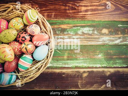 Easter eggs in various patterns and colors in a bird's nest placed on a wooden floor decorated in retro style. Stock Photo