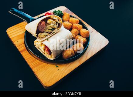 American style brunch burrito with scrambled eggs, sausages, hash brown, and tomatoes. Stock Photo