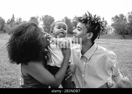 Happy African family enjoying a tender moment during the weekend outdoor - Mother and father having fun with their daughter in a public park Stock Photo