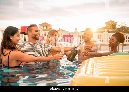 Happy friends toasting champagne at pool party - Young people having fun drinking sparkling wine in luxury tropical resort at sunset Stock Photo