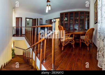 The second floor of the cottage with a staircase down, a wardrobe with books, a table and wicker chairs and doors to the bedrooms. Stock Photo