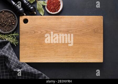 Kitchen cutting wooden board with spices and ingredients for cooking on black background. Space for text. View from above. Stock Photo
