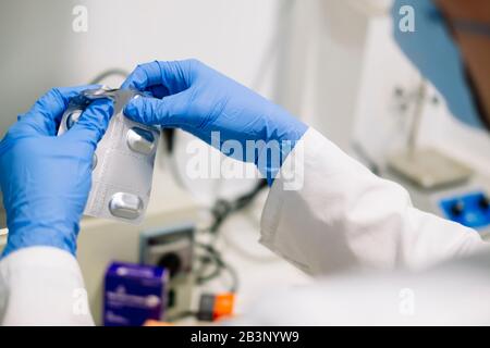 Closeup detail of the hands of a person in white coat taking some pills with blue latex gloves Stock Photo
