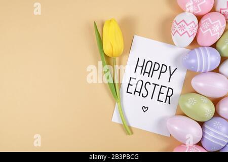 'Happy Easter' text card with colorful easter eggs and single yellow tulip spring flower on right side of yellow background with blank copy space Stock Photo