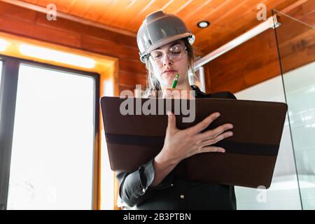 low angle portrait of a woman holding a clipboard as she taking notes during indoor air quality inspection, looking for molds or fungi on wooden walls Stock Photo