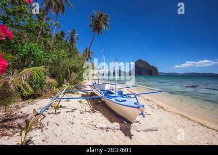 Colored banca boat and vibrant flowers at Las cabanas beach. Surreal landscape in background. Exotic nature scenery in El Nido, Palawan, Philippines Stock Photo