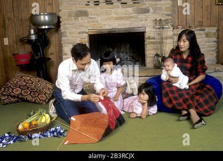 Austin Texas USA, circa 1988: Vietnamese-American family putting kite together at home. MR ©Bob Daemmrich Stock Photo