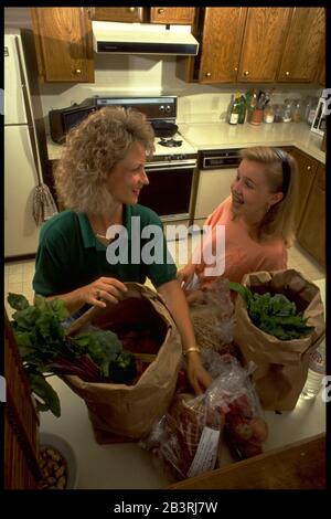 Austin Texas USA, circa 1990: Anglo mother and pre-teen daughter take groceries out of shopping bags in their kitchen after shopping at grocery store. ©Bob Daemmrich Stock Photo