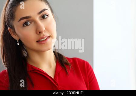 Portrait of young beautiful brunette woman in red shirt in office Stock Photo