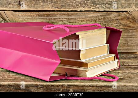 Stack of old books in pink paper bag on wooden background with copy space. World book day is April 23 Stock Photo