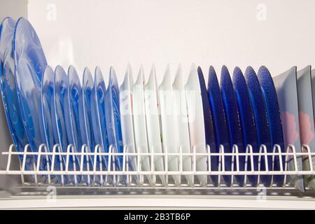 Plates of different colors in Dish dryer in the closet on white background. Stock Photo