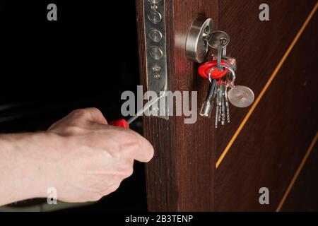 Close up of hands of young carpenter holding a screwdriver and fixing the lock of door. The man is standing in workwear. Stock Photo
