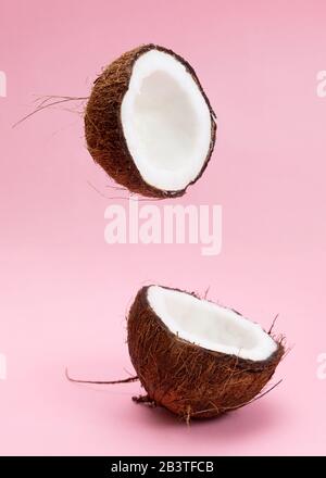 Two coconut section halves isolated on pink background one broken in two. Levitation composition. Stock Photo