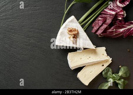 Delicious brie cheese on black background. Brie type of cheese. Camembert. Fresh Brie cheese and a slice on stone board. Italian, French cheese. Stock Photo