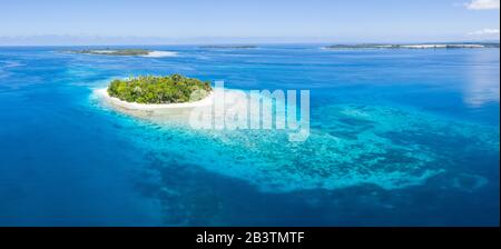 An idyllic tropical island is surrounded by reef in the Halmahera Sea, Indonesia. This remote region is part of the heart of the Coral Triangle. Stock Photo