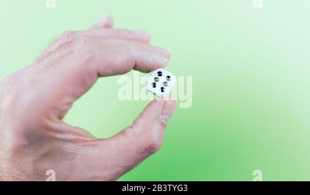 close up of hand holding dice showing showing six pips against green background Stock Photo