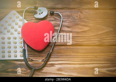 A heart with a stethoscope lies on a wooden background. Healthy heart. Stock Photo