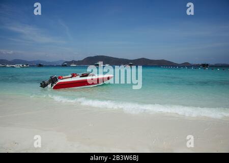 A motorboat on the azure shore. The red boat. Boat on the sandy shore. Stock Photo